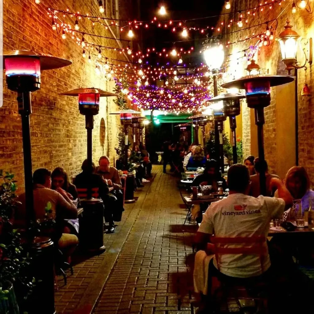 Outdoor dining area with string lights and patio heaters at night.