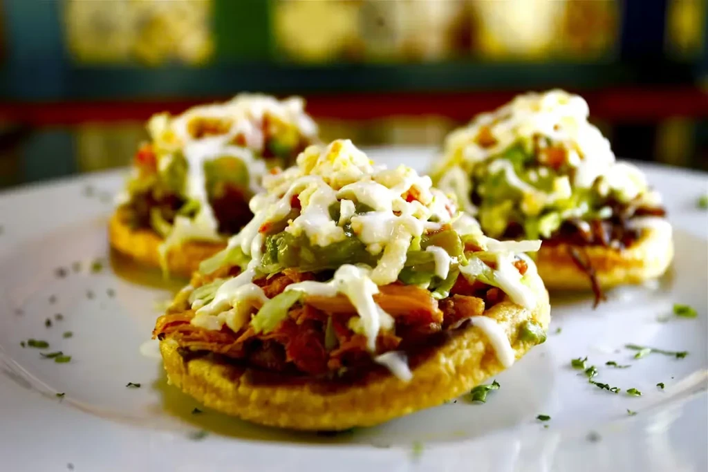 Three sopes with meat, lettuce, avocado, cheese, and cream.