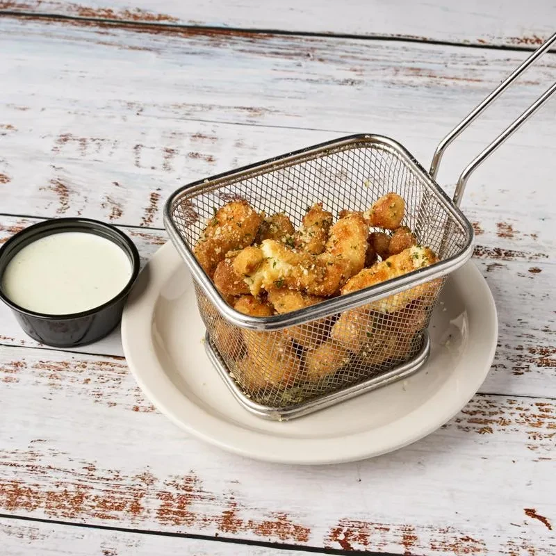 Fried cheese curds in a basket with a side of dipping sauce.