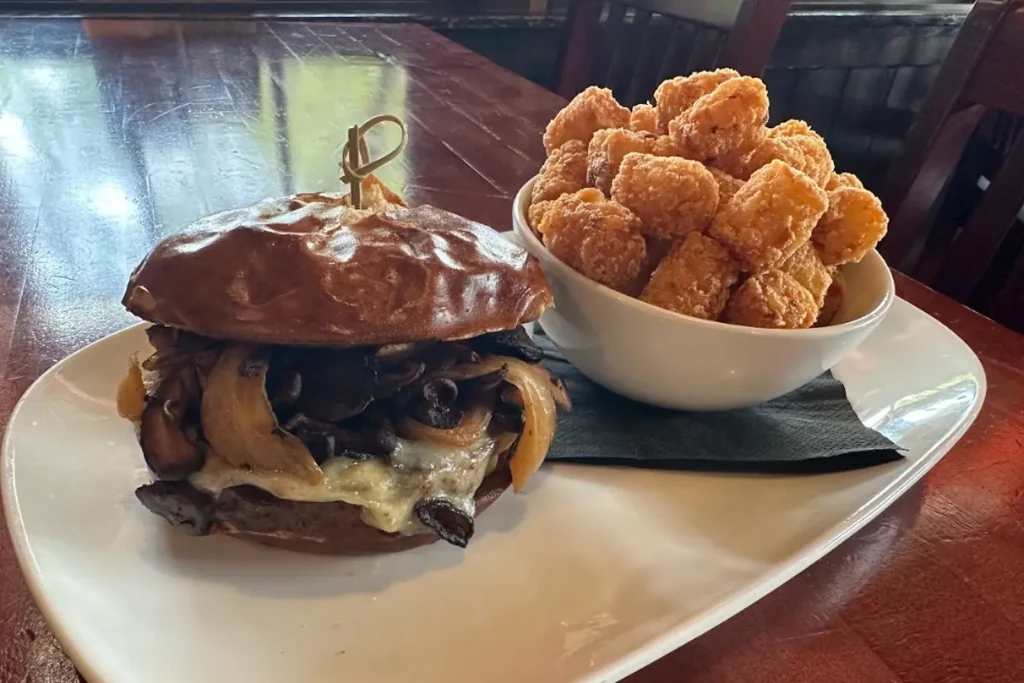 Close-up: Burger with onions, mushrooms, melted cheese, and tater tots.