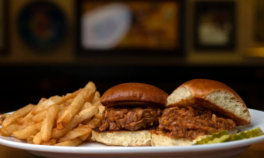 Two pulled pork sliders, french fries, and pickle slices on a plate.