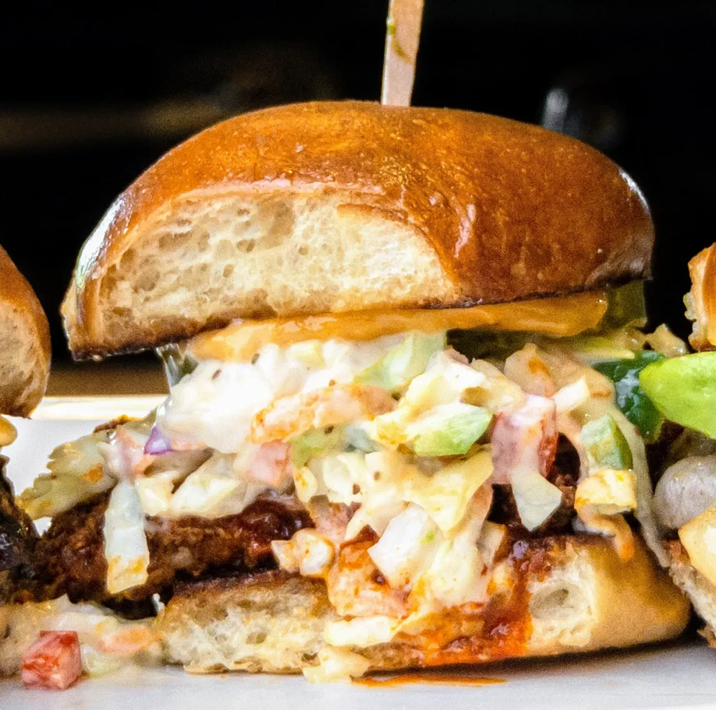 Gourmet burger with fried patty, coleslaw, and red sauce.
