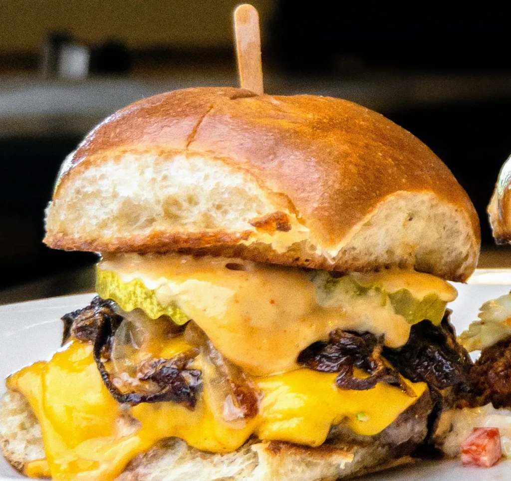 Side profile of a burger with melted cheese, pickles, and sauce.