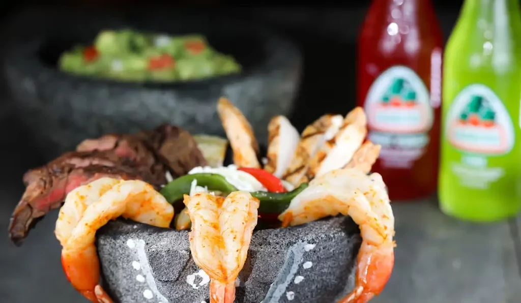 Grilled shrimp, steak, and chicken in a molcajete with guacamole.