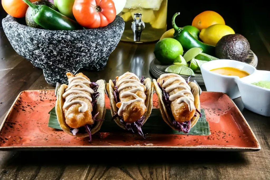 Three fried fish tacos with cabbage and sauce on a plate.
