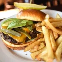 Cheeseburger with avocado, pickles, and golden french fries on a plate.