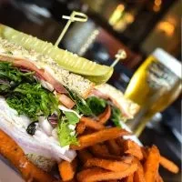 Stacked deli sandwich with pickle spear and sweet potato fries.