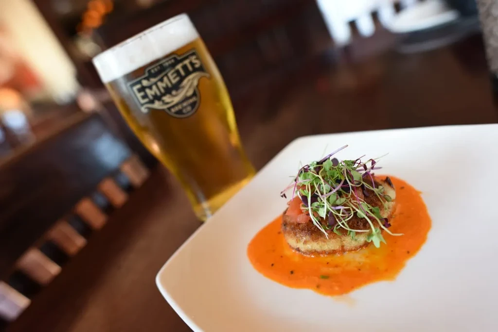 Plated golden-brown patty, microgreens, and beer on dark wood.