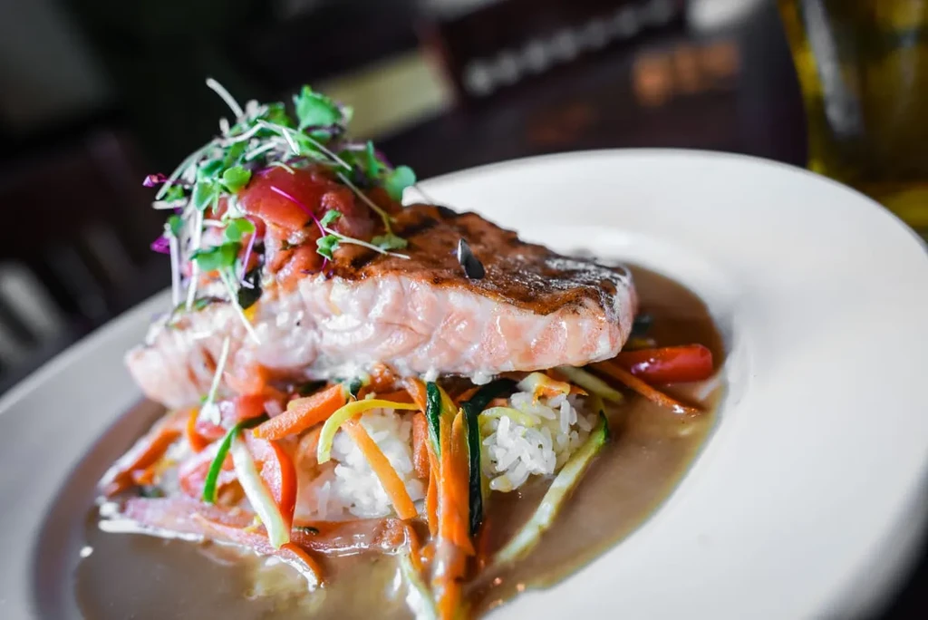 Seared salmon with rice, julienned vegetables, microgreens, and brown sauce.