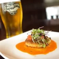 Pan-seared patty in orange-red sauce, microgreens, blurred Emmett's beer.