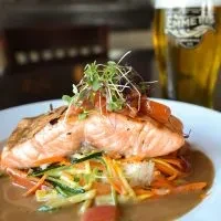 Plated salmon fillet with microgreens, vegetables, and blurred beer glass.