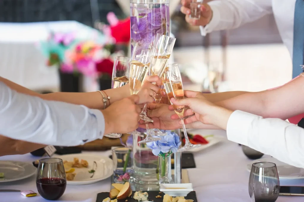 Hands toast champagne flutes over a dinner table.