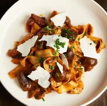 Pasta with mushroom sauce, shaved cheese, and herbs on a white plate.