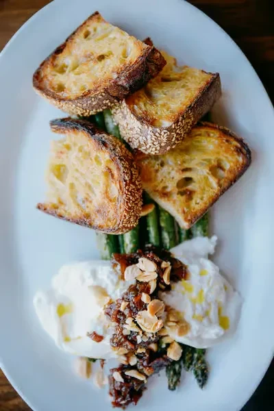 Toasted bread with asparagus, burrata, almonds, and a red topping.