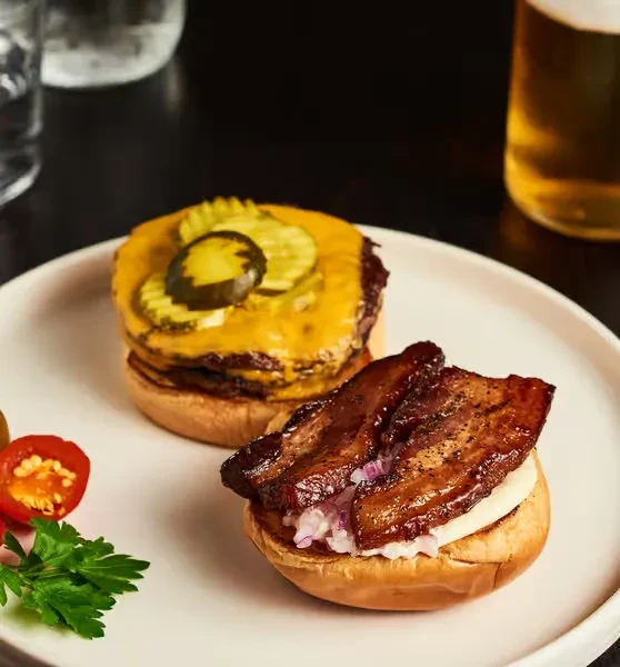Two open-faced burgers with cheese, bacon, pickles, and onion.