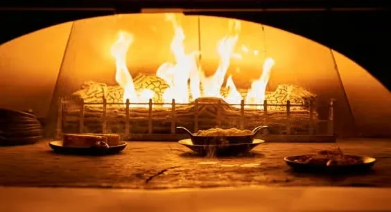 Three dishes on a hearth with flames from a wood-fired oven.