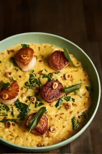 Overhead shot of seared scallops on a creamy risotto with greens and nuts.