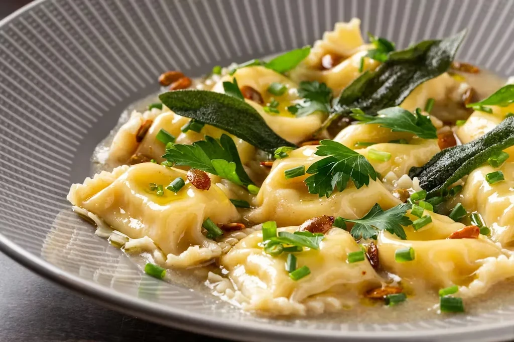 Close-up of ravioli garnished with fresh herbs in a light sauce.