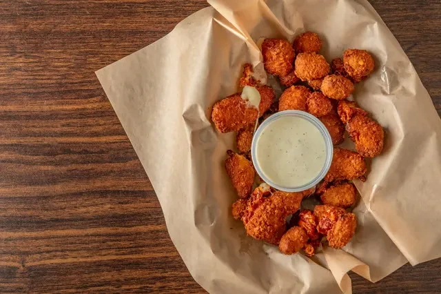 Top-down view of fried cheese curds with dipping sauce on parchment paper.