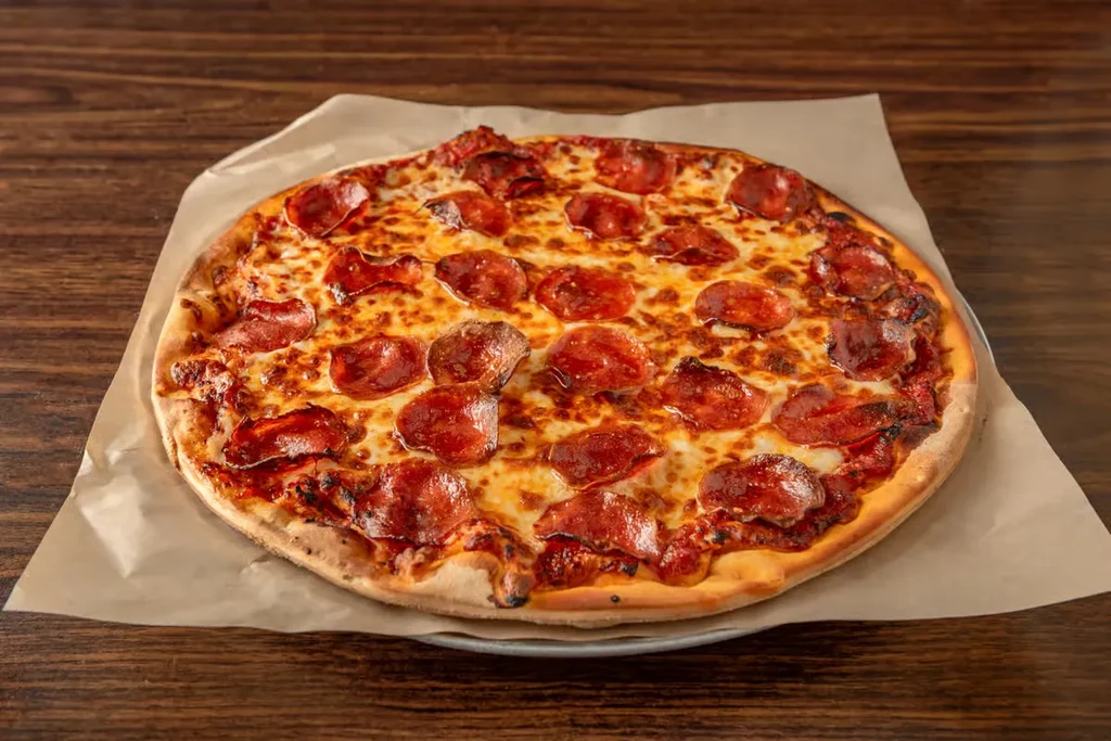 Freshly baked pepperoni pizza on parchment paper and a wooden table.