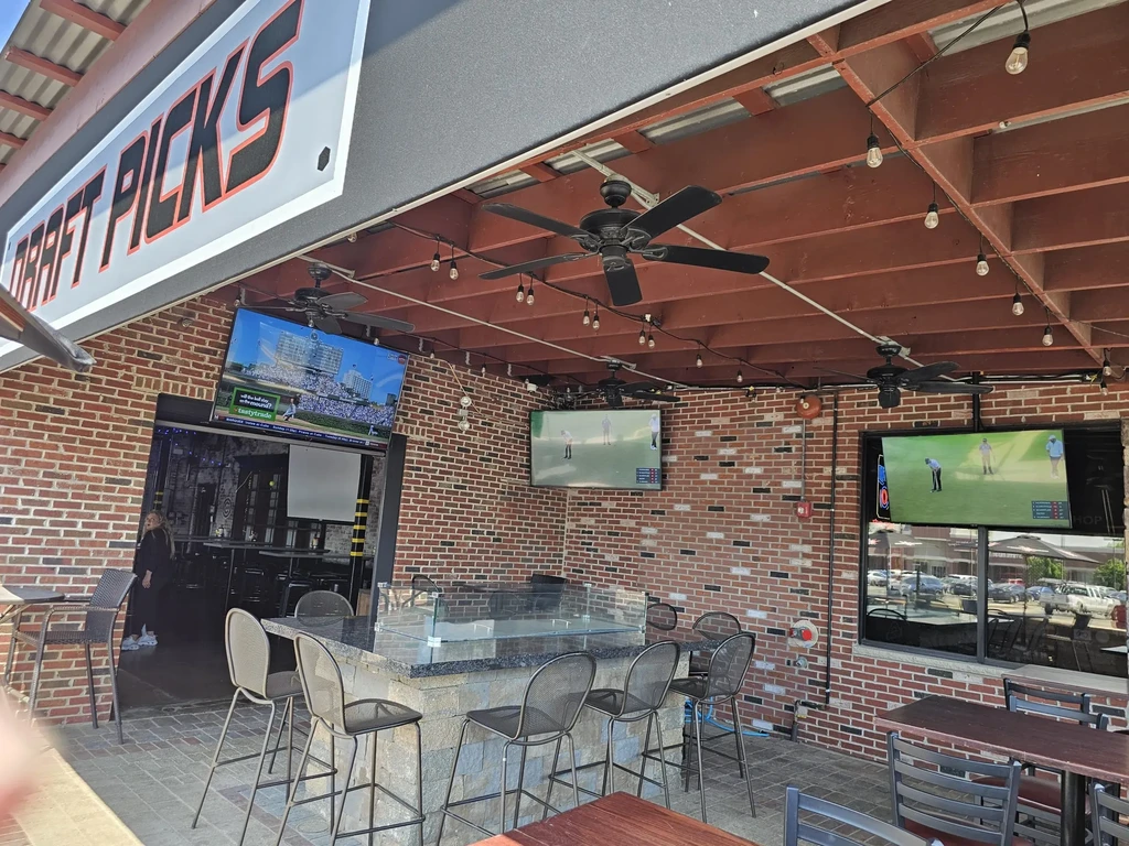 Outdoor sports bar patio with high-top seating and TVs.