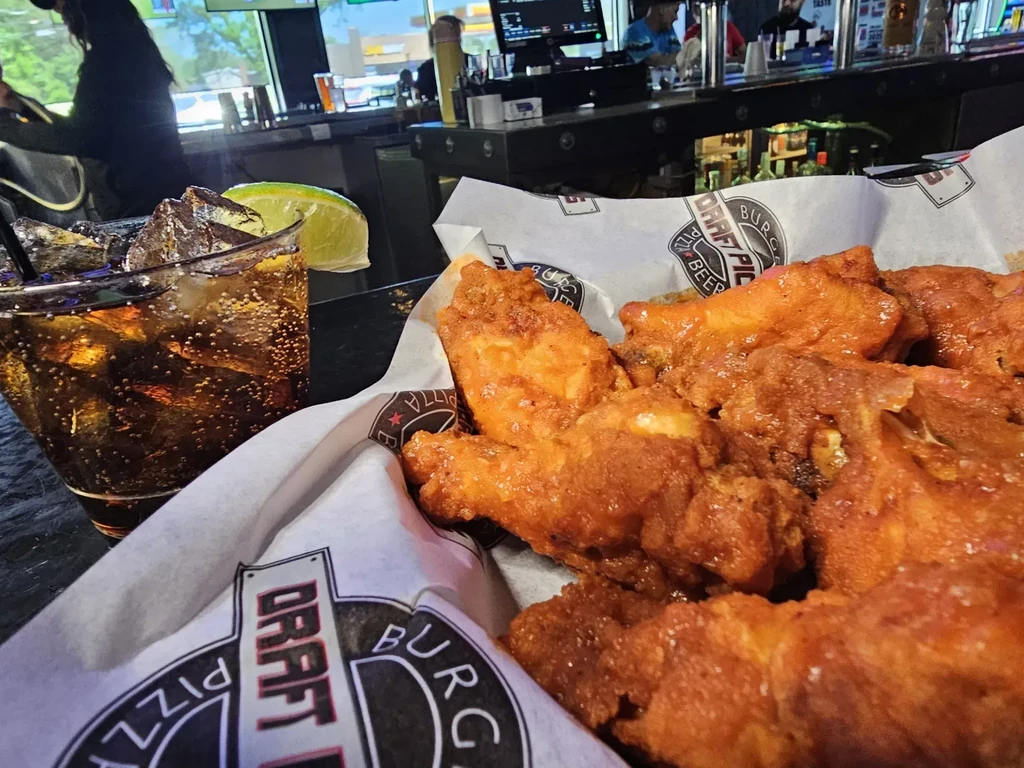 Basket of chicken wings and a drink on a dark surface.