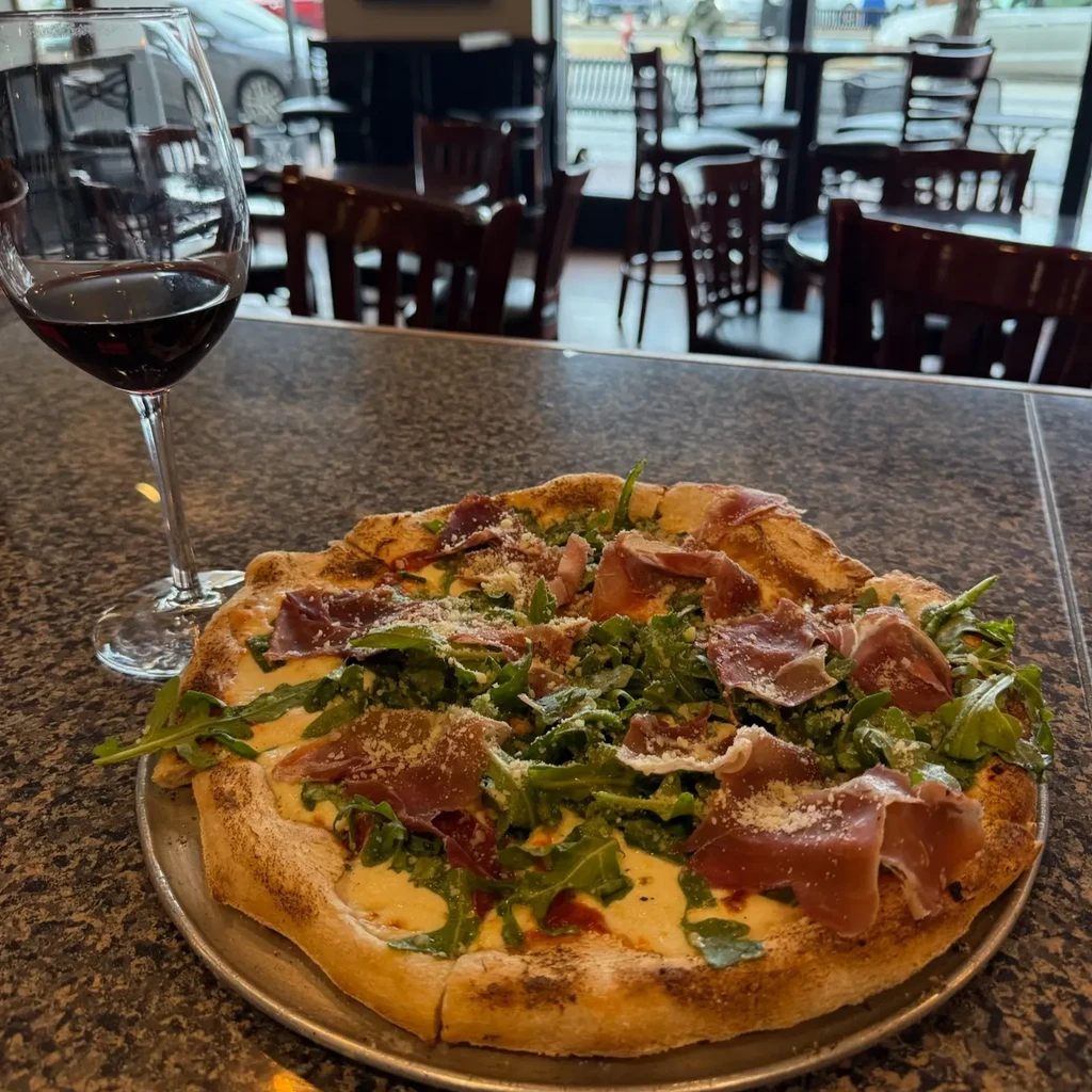 Gourmet pizza with prosciutto and arugula, and a glass of red wine.