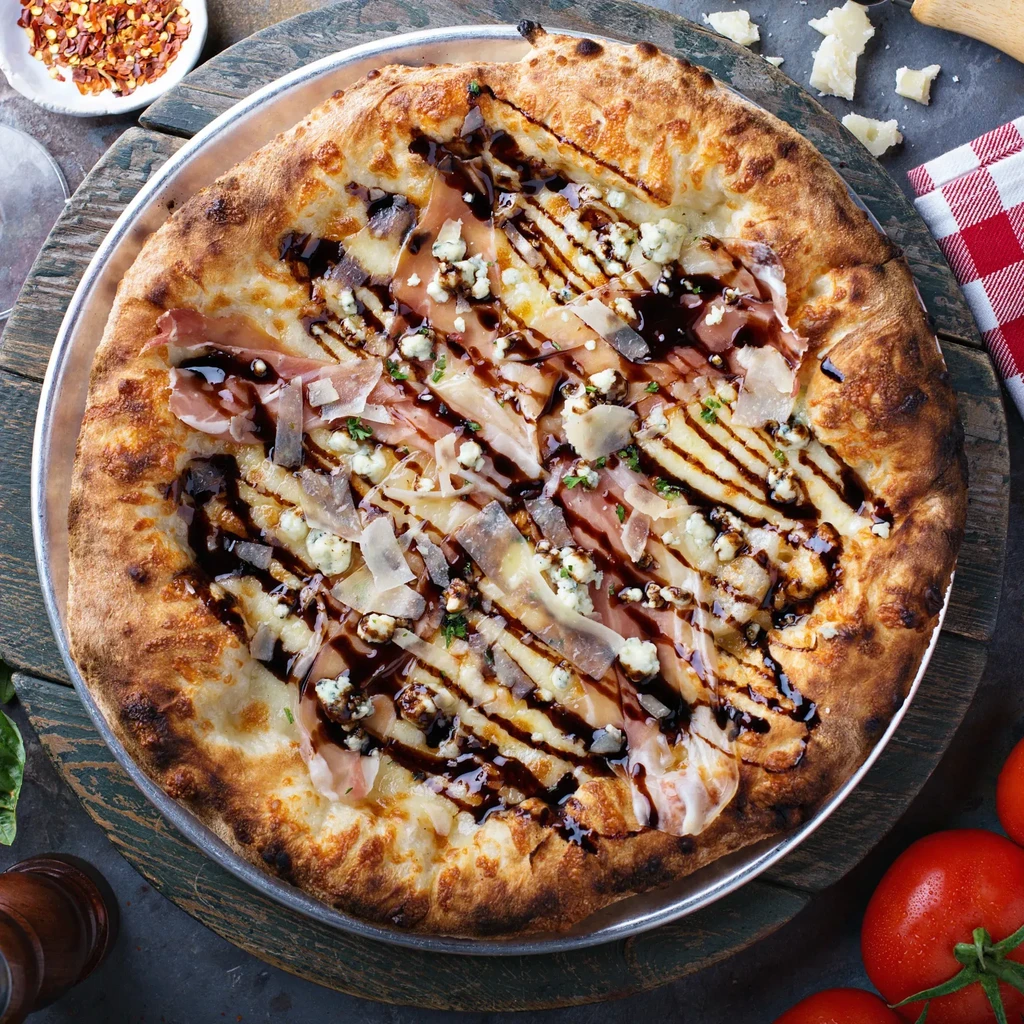 Gourmet pizza with prosciutto, Parmesan, blue cheese, and balsamic glaze.