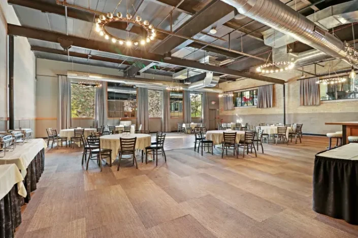 Empty industrial-chic banquet hall with tables, buffet, bar, and chandeliers.