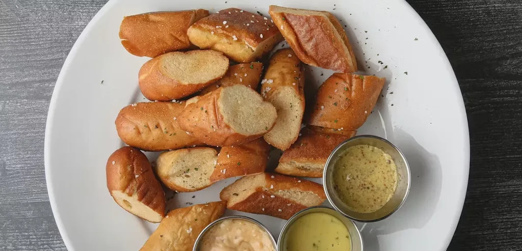 Plate of golden-brown pretzel pieces with three assorted sauces.