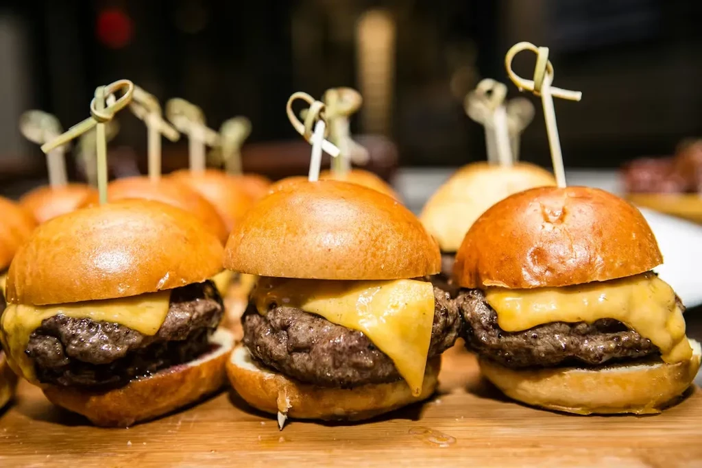 Close-up of mini cheeseburger sliders with melted cheese on a wooden board.