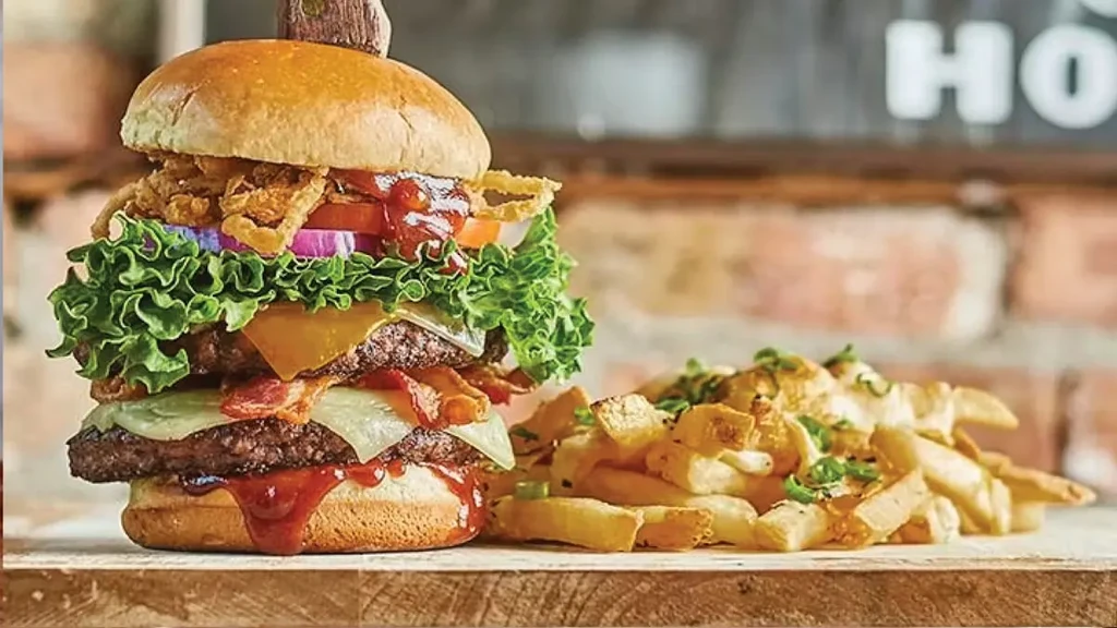 A large, stacked burger with fries on a rustic wooden surface.