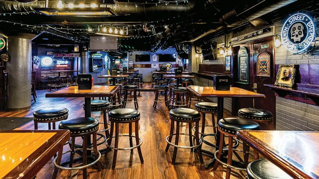 Rustic bar interior, empty, with high-top tables, industrial details, and brand signs.