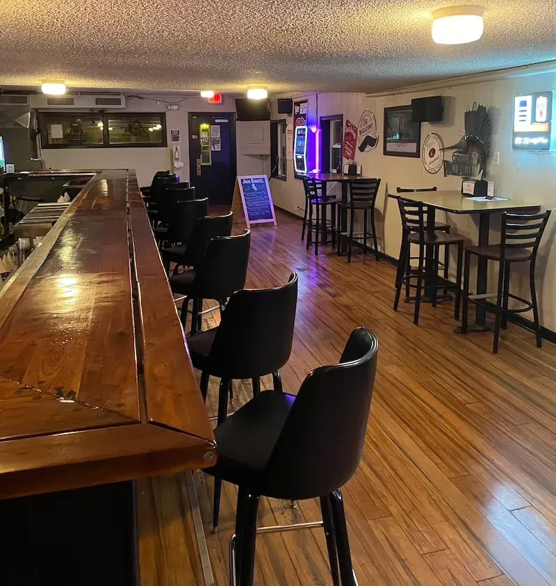 Empty bar interior featuring a wooden counter, high-top tables, and decor.