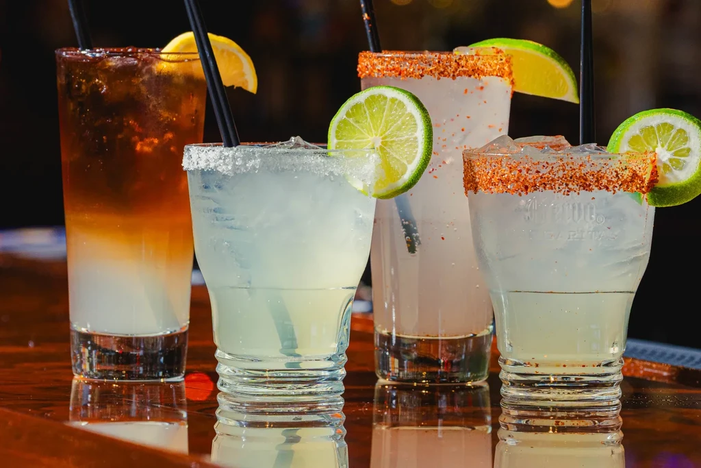 Four cocktails, including Topo Chico and Jarritos, on a reflective bar.