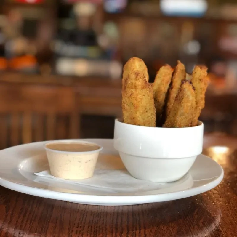 Golden-brown fried pickles and dipping sauce on a wooden table.