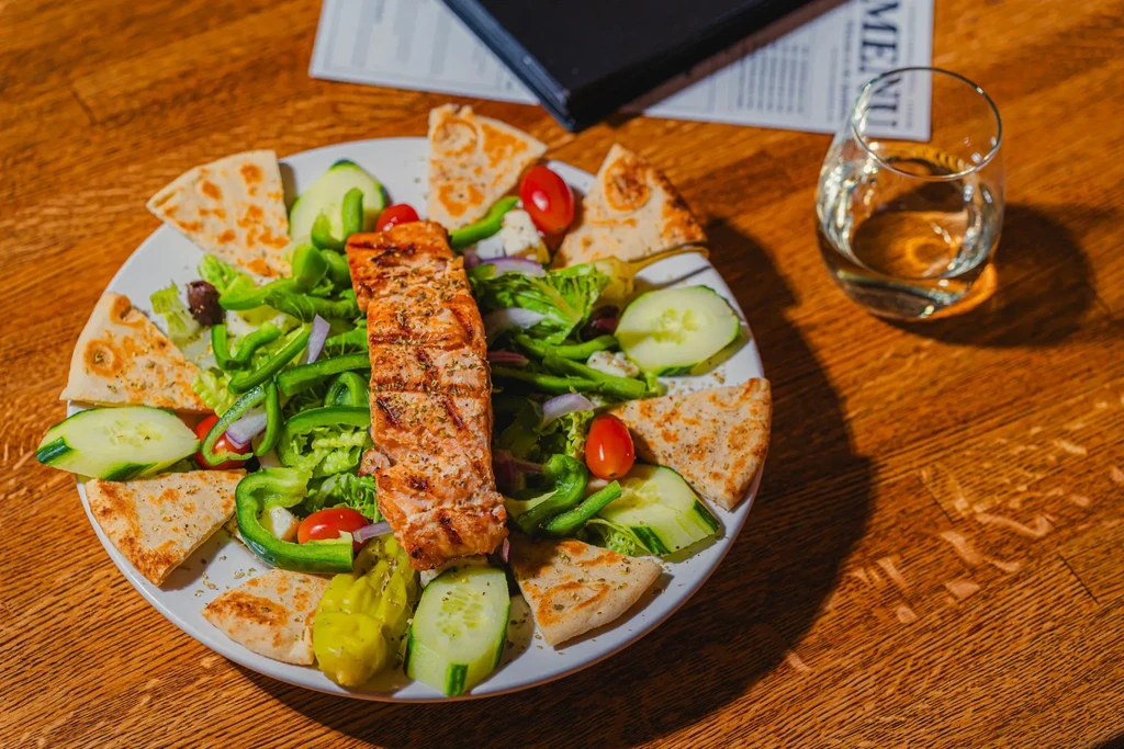 Grilled salmon salad with pita bread on a wooden table.