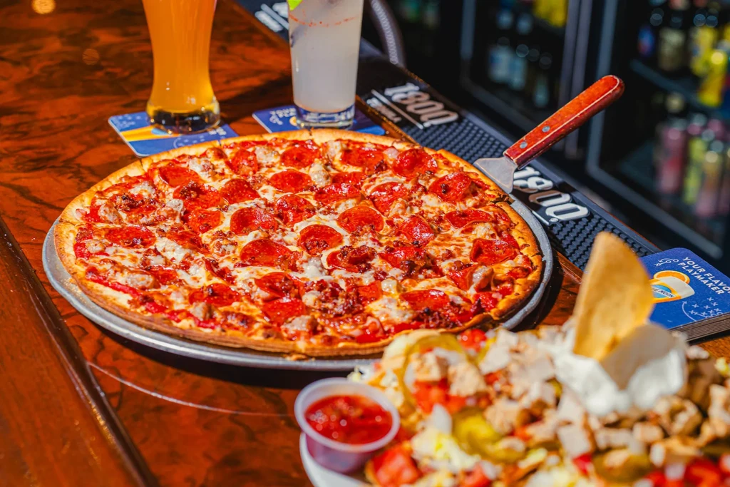 Pepperoni pizza, nachos, beer, and a mixed drink on a bar.