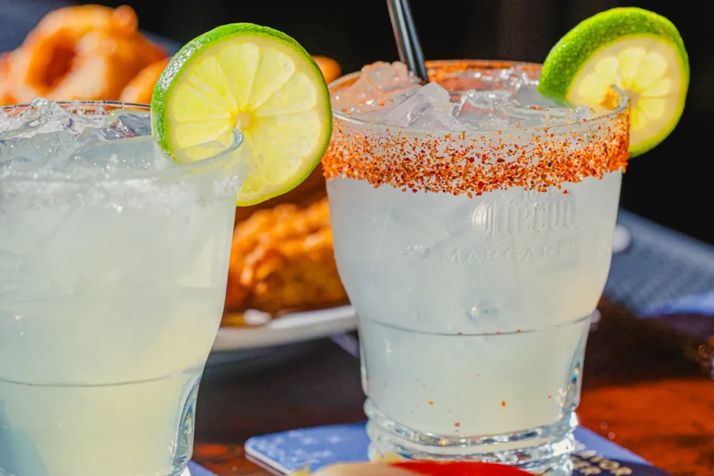 Icy margarita with chili-lime rim and lime, next to another drink.
