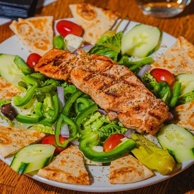 Close-up of grilled salmon, vibrant green salad, and pita bread.