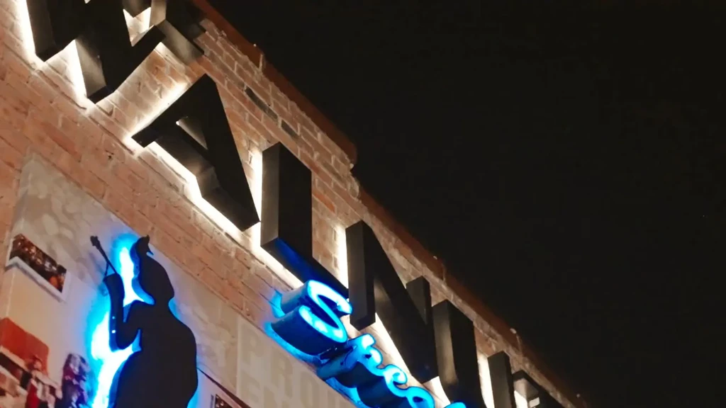 Backlit "WALN" sign and blue-lit silhouette on a nocturnal brick building.