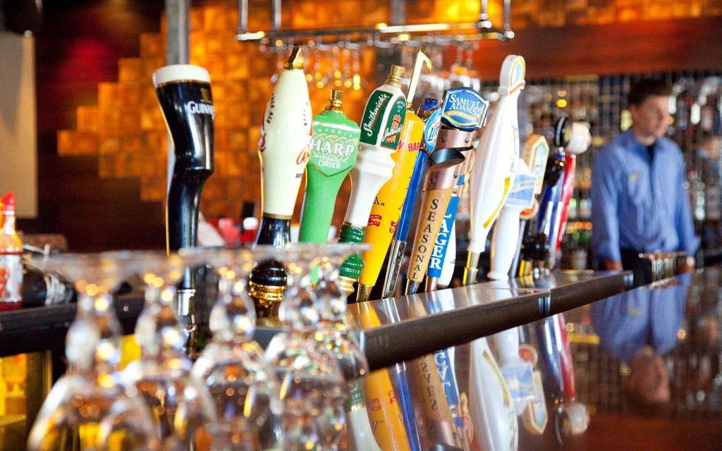 Various branded beer taps and inverted martini glasses at a bar.