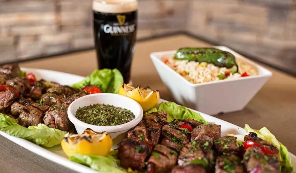 Grilled meat skewers with sauce, rice with chili, and a Guinness beer.