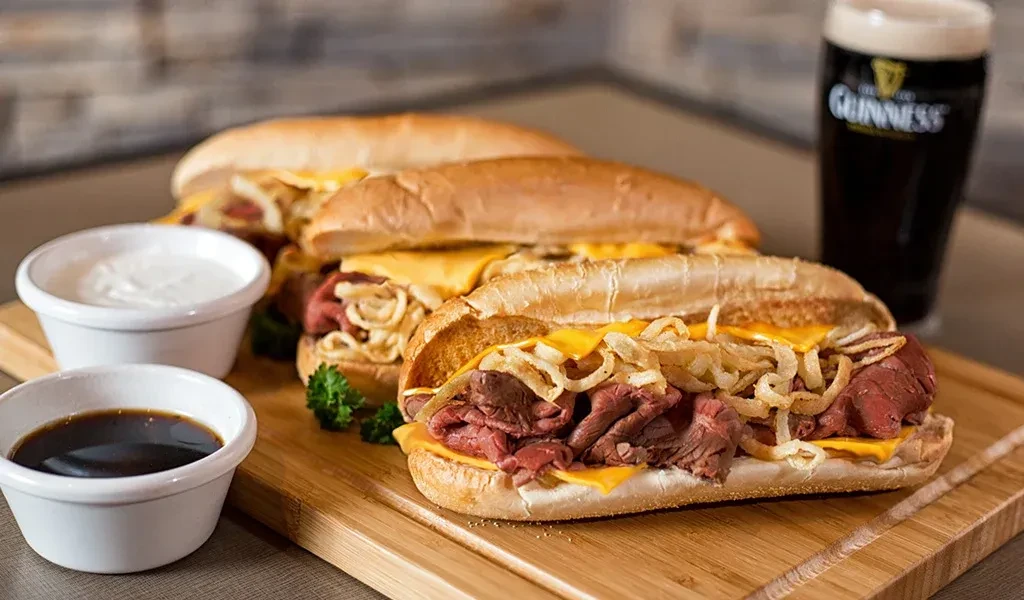 Roast beef subs with melted cheese, fried onions, sauces, and Guinness.