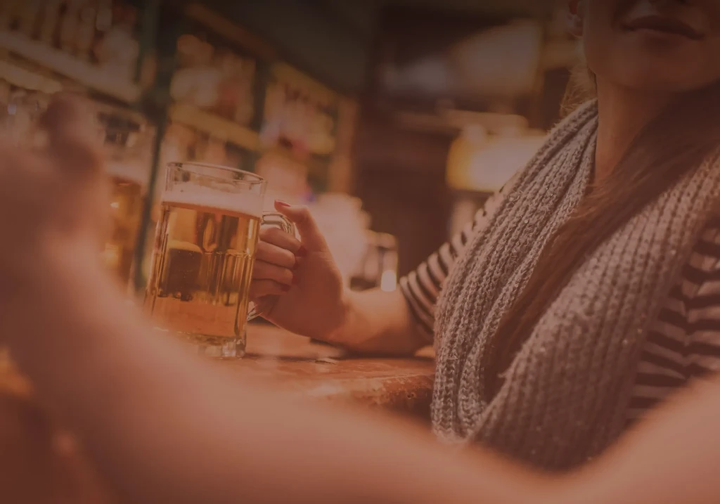 Hand with red nails holds a golden beer mug at a bar.
