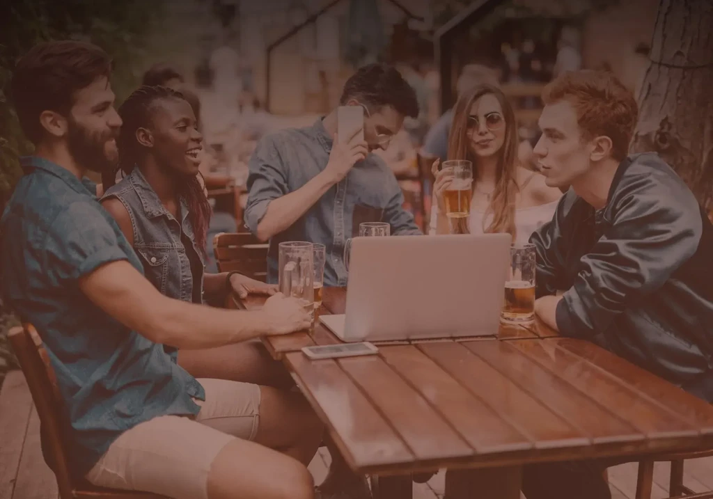 Five young adults socializing with beer and tech on a dim patio.