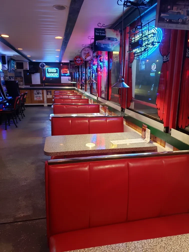 Empty retro diner interior with red booths and colorful neon lights.