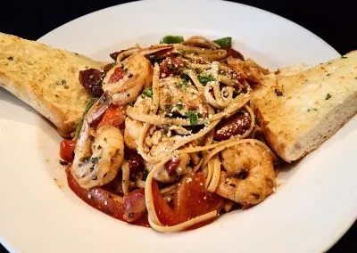 Close-up of shrimp linguine with peppers, cheese, herbs, and garlic bread.