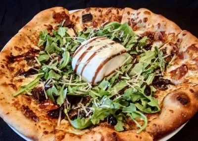 Close-up, top-down pizza with burrata, balsamic glaze, and arugula.