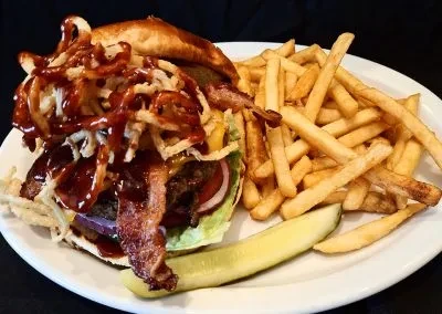 Stacked burger with bacon, onion strings, golden fries, and pickle.